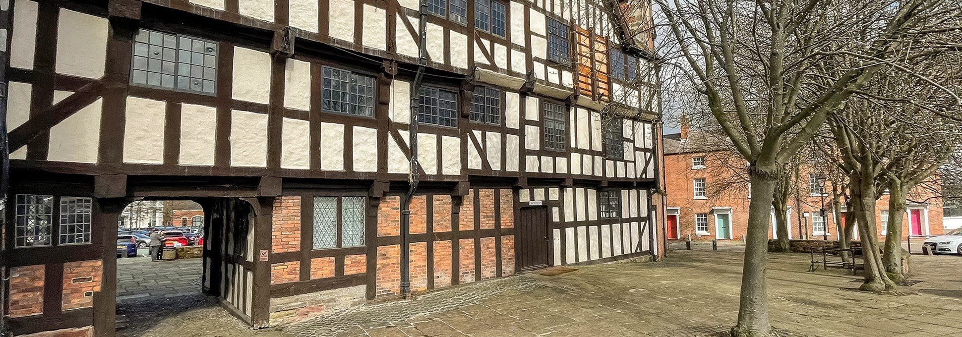 A timber-framed four-storey building with brick ground floor in a flagstone courtyard